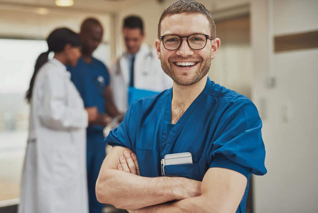 Smiling optimistic young male hospital surgeon standing in front of his colleagues