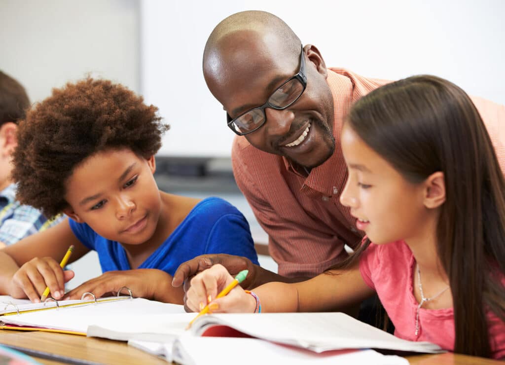 Teacher Helping Pupils Studying At Desks In Classroom